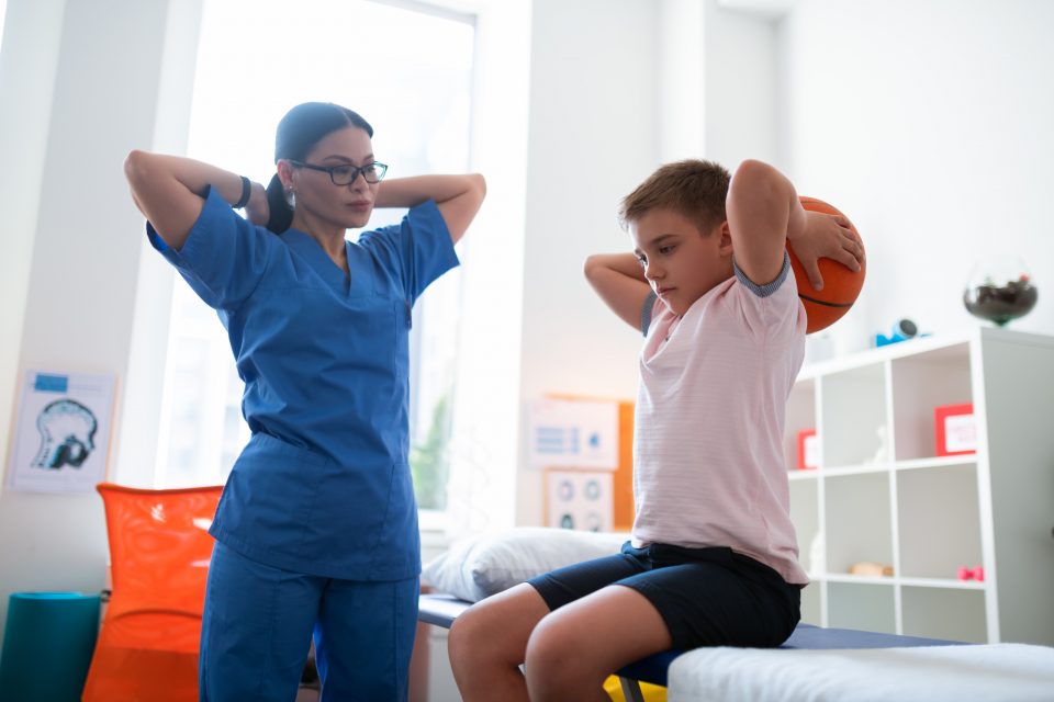 Serious diligent young boy putting ball over head while stretching muscles