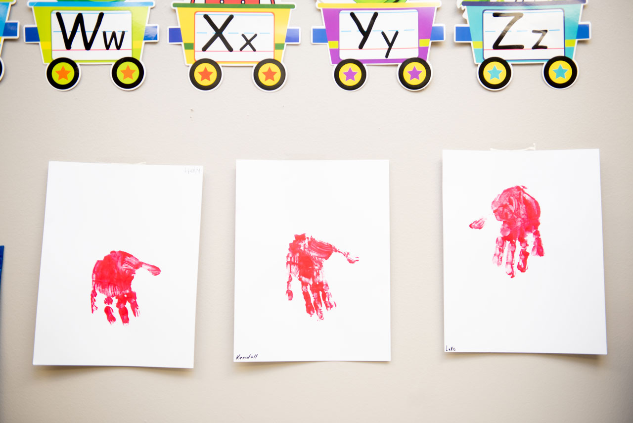 Three pieces of paper with a paint handprint on each hung on the wall at Carolina Therapeutics Academy
