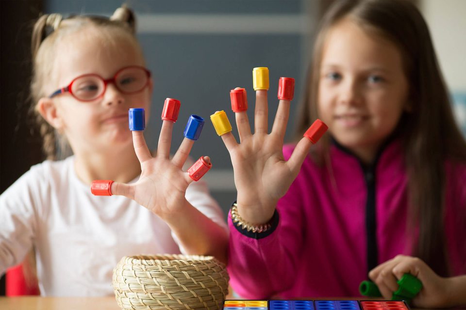 Two young girls hold up their hands with little colored plastic pieces on each finger