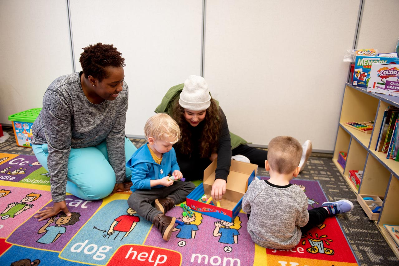Two preschool teachers playing on the carpet with two young boys at therapeutic day school