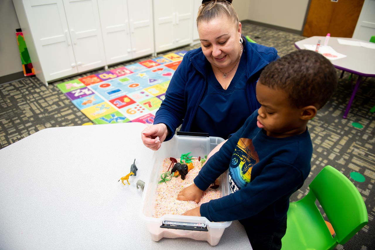 Young boy undergoing sensory therapy with his hands in a bin of rice with small animal figurines at special needs preschool Carolina Therapeutics Academy in Rock Hill, SC