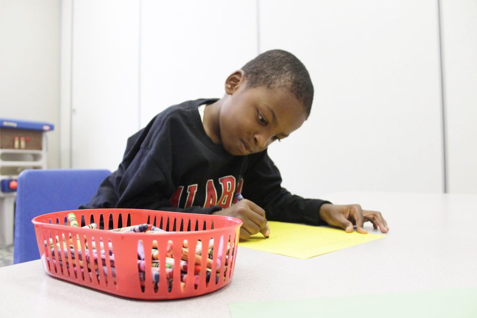 A young boy sitting and drawing with crayons at a table at Carolina Therapeutics Academy in Rock Hill, SC