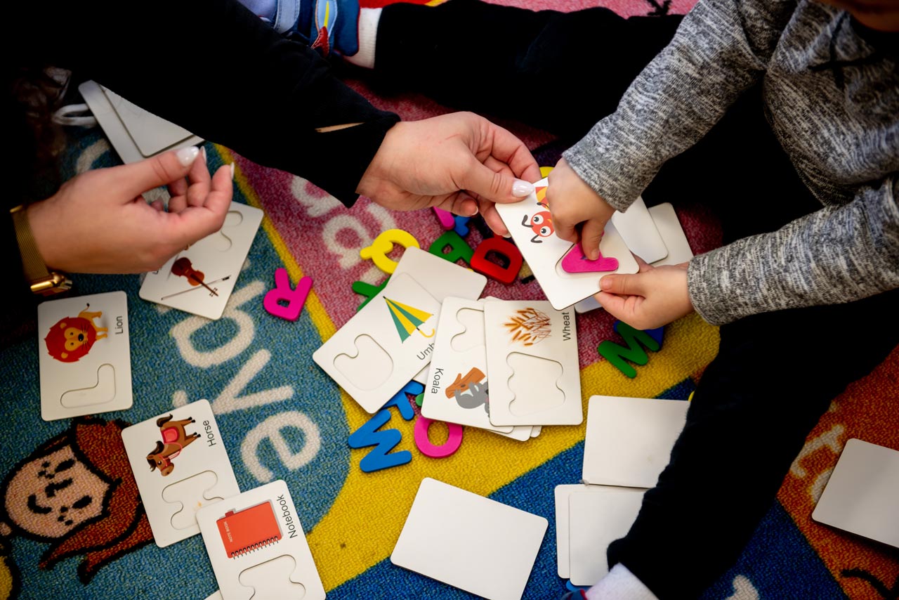 Young child holding an alphabet card with an instructor