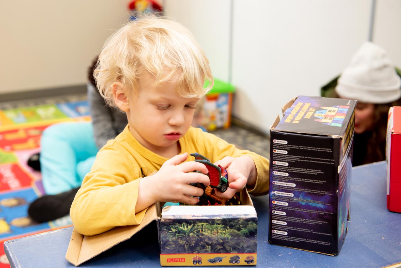 Young boy with blonde hair unboxes a toy car at special needs after school program