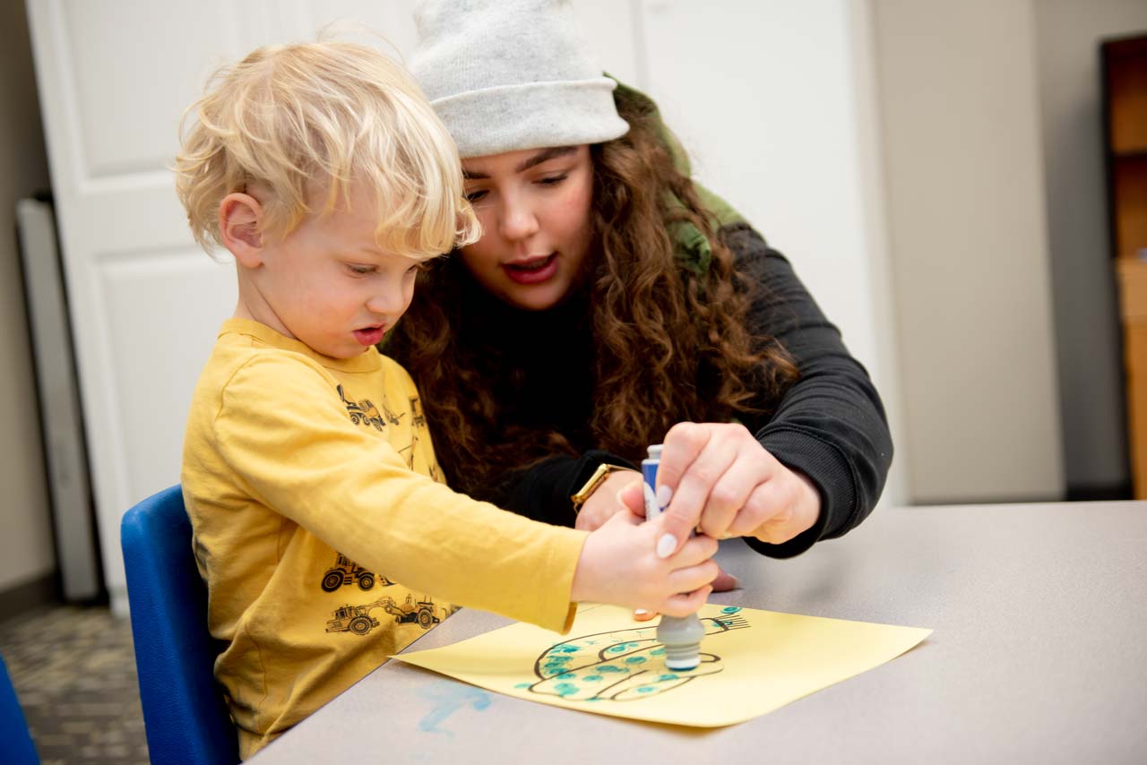 Young boy wearing a yellow shirt using a marker to color a picture at special needs preschool