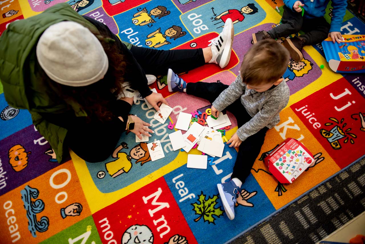 Young boy sitting on carpet with an instructor playing with alphabet cards at special needs preschool Carolina Therapeutics Academy in Rock Hill, SC